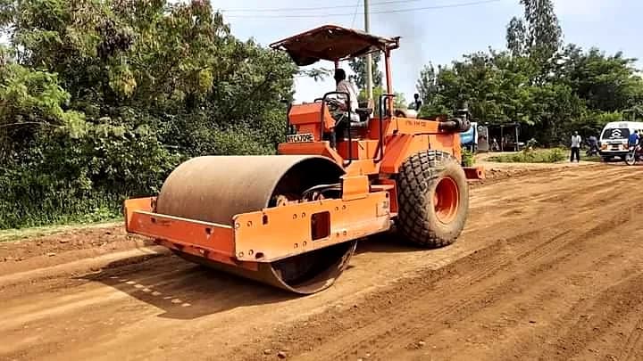 Heavy vibratory roller compacting road sub-base ahead of asphalt paving